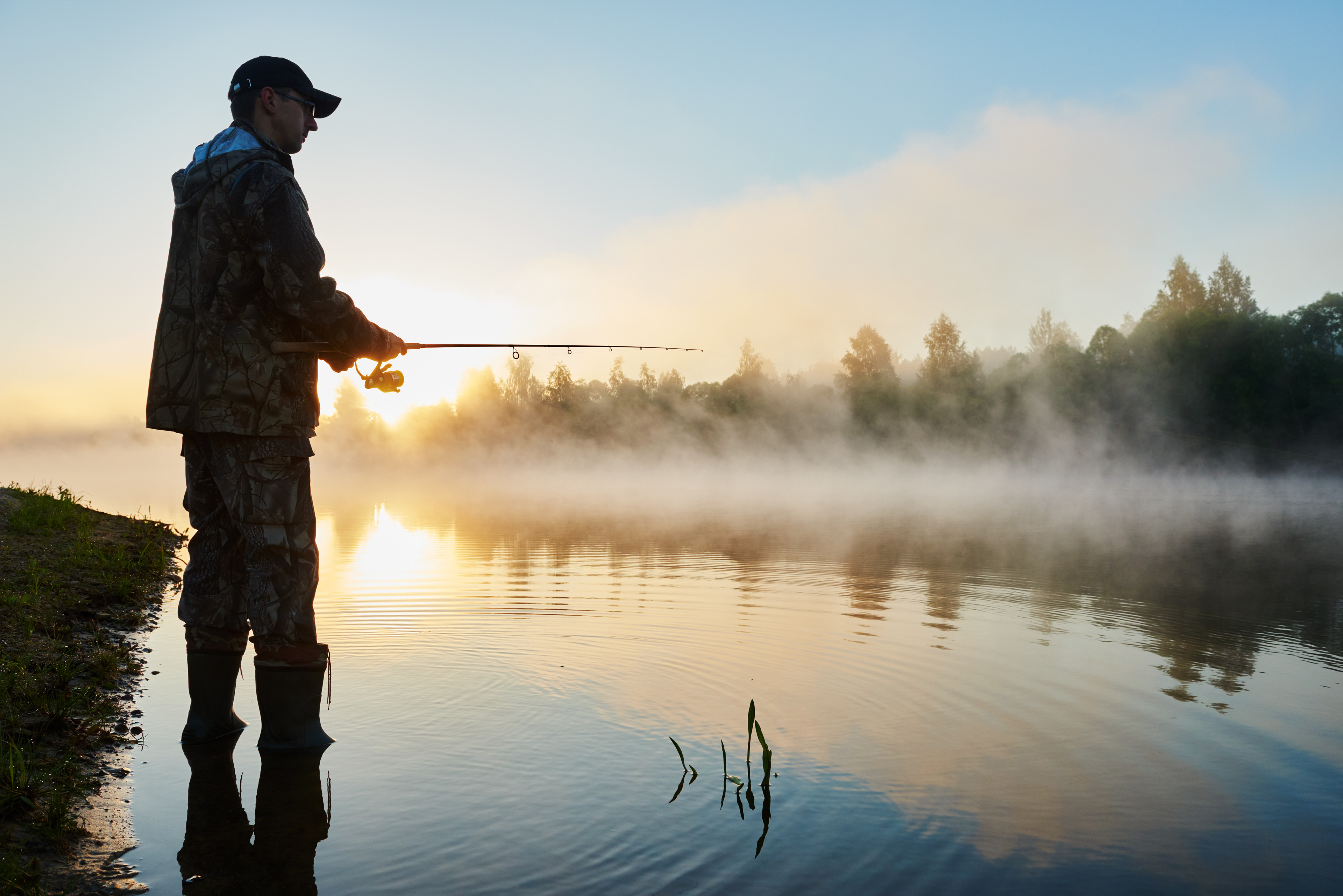 Man standing in river with fishing rod.